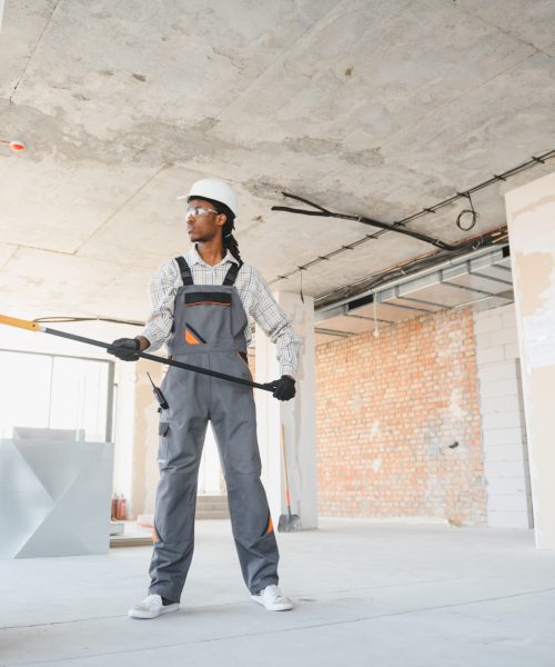 Construction worker painting wall with roller in building under construction