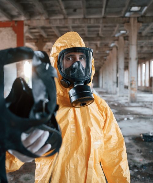Giving the respirator. Man dressed in chemical protection suit in the ruins of the post apocalyptic building.