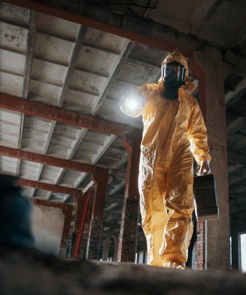 Using the flashlight. Man dressed in chemical protection suit in the ruins of the post apocalyptic building.